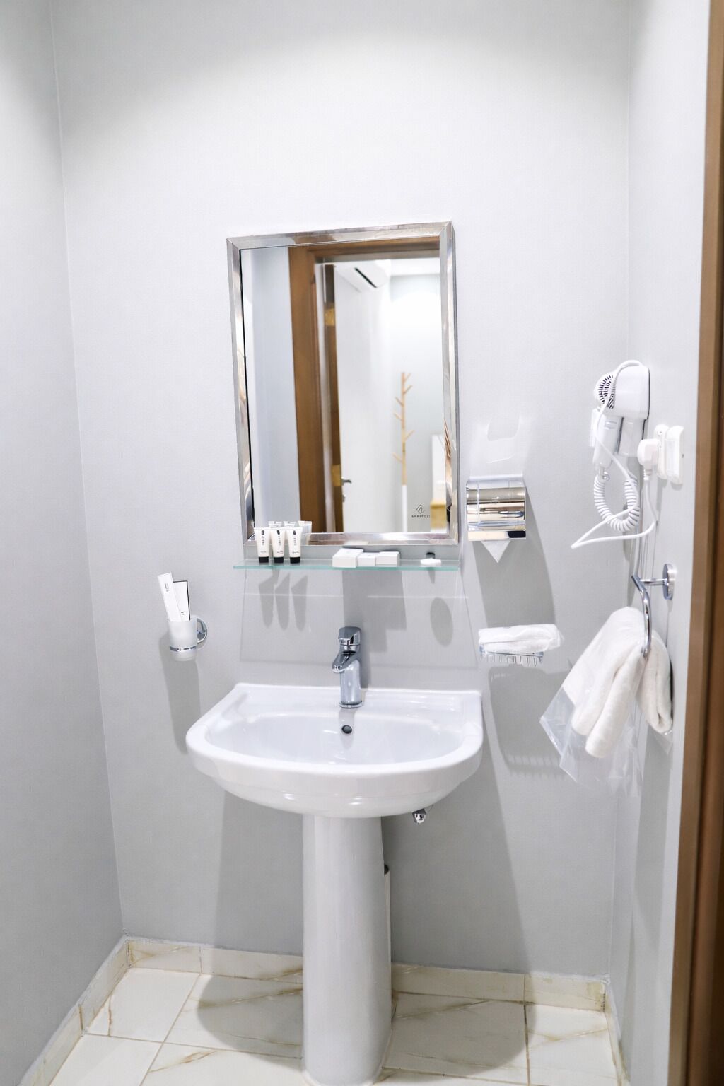 Ein modernes Badezimmer mit einem weißen Waschbecken, einem Spiegel und einem Fön an der Wand.