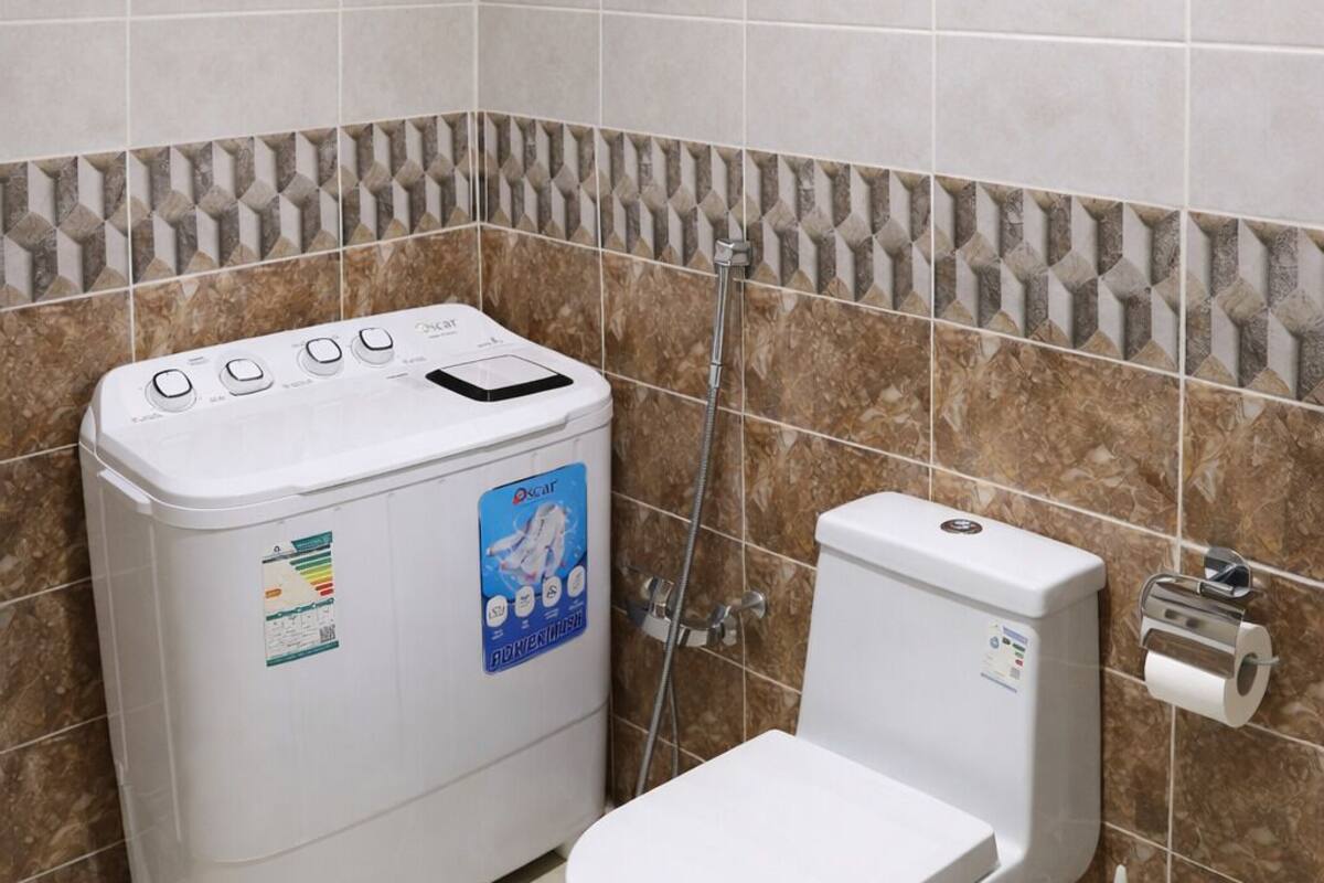Een badkamer met een wit toilet, een witte wasmachine, een douche en een handdoekhouder.