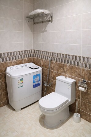 Ein Badezimmer mit Toilette, Waschmaschine, Dusche und Handtuchhalter.