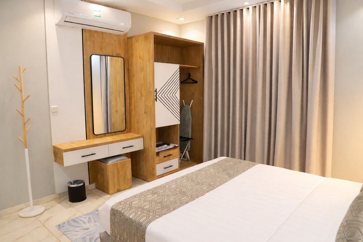 Une chambre d’hôtel moderne dotée d’un grand lit, d’une coiffeuse en bois avec un miroir, d’un porte-vêtements et d’une armoire intégrée.