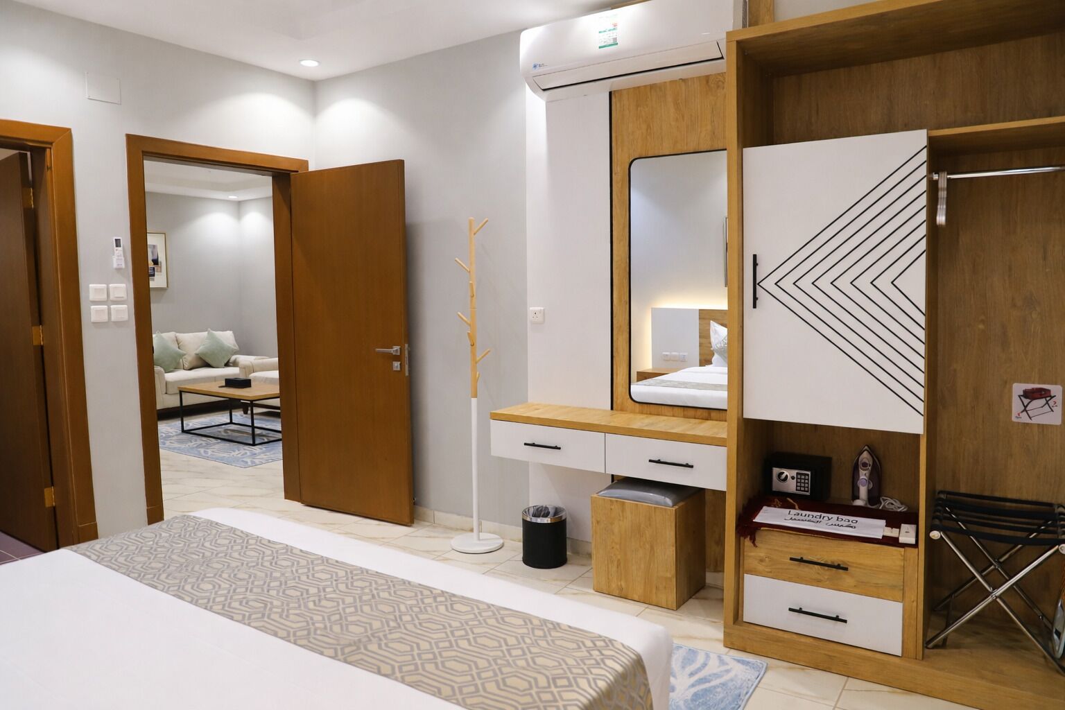 Een moderne hotelkamer met een bed, een houten garderobe, een spiegel, een nachtkastje en een klein bureau met een stoel.