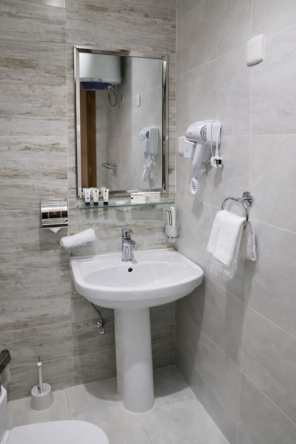 Une salle de bain moderne avec un lavabo blanc, un miroir, un sèche-cheveux et un porte-serviettes.