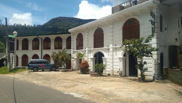 Um edifício com fachada branca e janelas emolduradas por vermelho, um caminho de entrada pavimentado e um carro estacionado.
