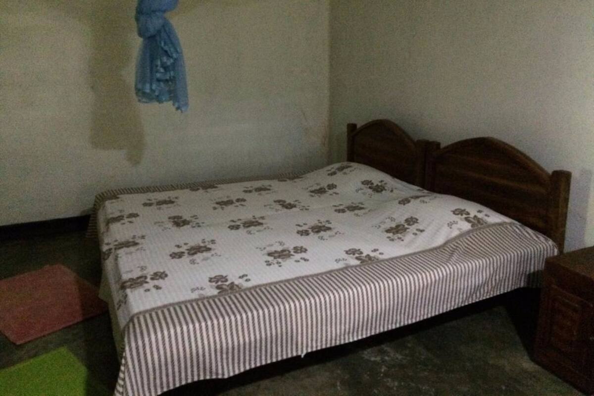 A small, single-bed room with a wooden headboard, a floral-patterned bedspread, and a striped blanket.