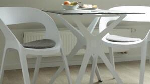 A modern dining area with a white table and chairs, a bowl of fruit, and a radiator in the background.