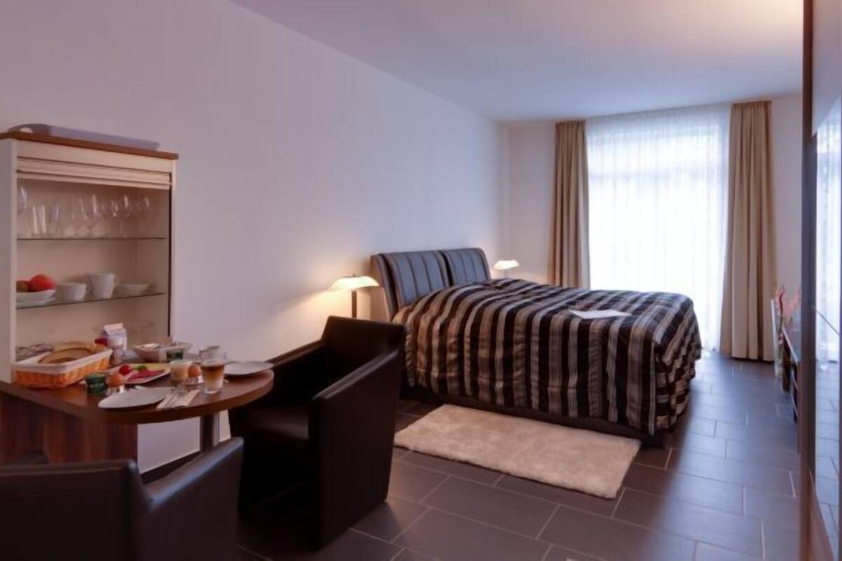 Ein Hotelzimmer mit Bett, Schreibtisch mit Stuhl, einem kleinen Tisch mit Frühstücksangeboten und einem Kleiderschrank.