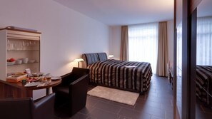 A hotel room with a bed, a desk with a chair, a small table with breakfast items, and a wardrobe. - Campus Boardinghouse Aachen (Aachen)