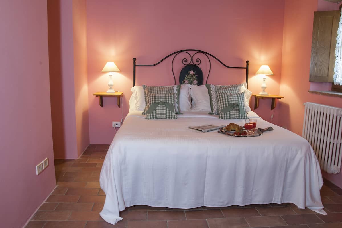 A bedroom with a bed, two bedside lamps, a radiator, and a breakfast tray on the bed.