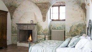 A bedroom with a fireplace, a bed with checkered bedding, and a mural on the walls. - Croce di Bibbiano (Colle di Val d'Elsa)