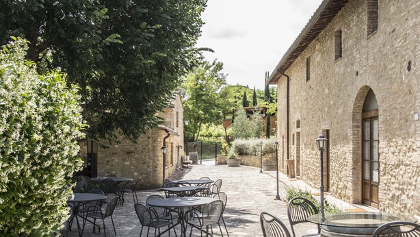 An outdoor patio area with stone tables and chairs, surrounded by stone walls and greenery. - Croce di Bibbiano (Colle di Val d'Elsa)