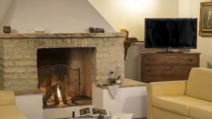 A cozy living room with a stone fireplace, a television, a sofa, and a coffee table with books and a chessboard. - Croce di Bibbiano (Colle di Val d'Elsa)