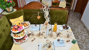 A dining table set with a variety of food and drinks, surrounded by green upholstered chairs. - Haus Elisabeth (Muehlbach Am Hochkoenig)