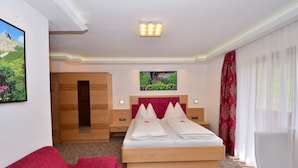 A hotel room with a large bed, a red sofa, a wooden wardrobe, and a painting of a mountain landscape. - Haus Elisabeth (Muehlbach Am Hochkoenig)