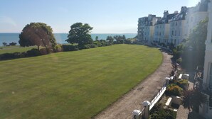 A grassy area with a pathway leading to a building with multiple balconies overlooking a body of water. - Westward Ho Hotel (Folkestone)
