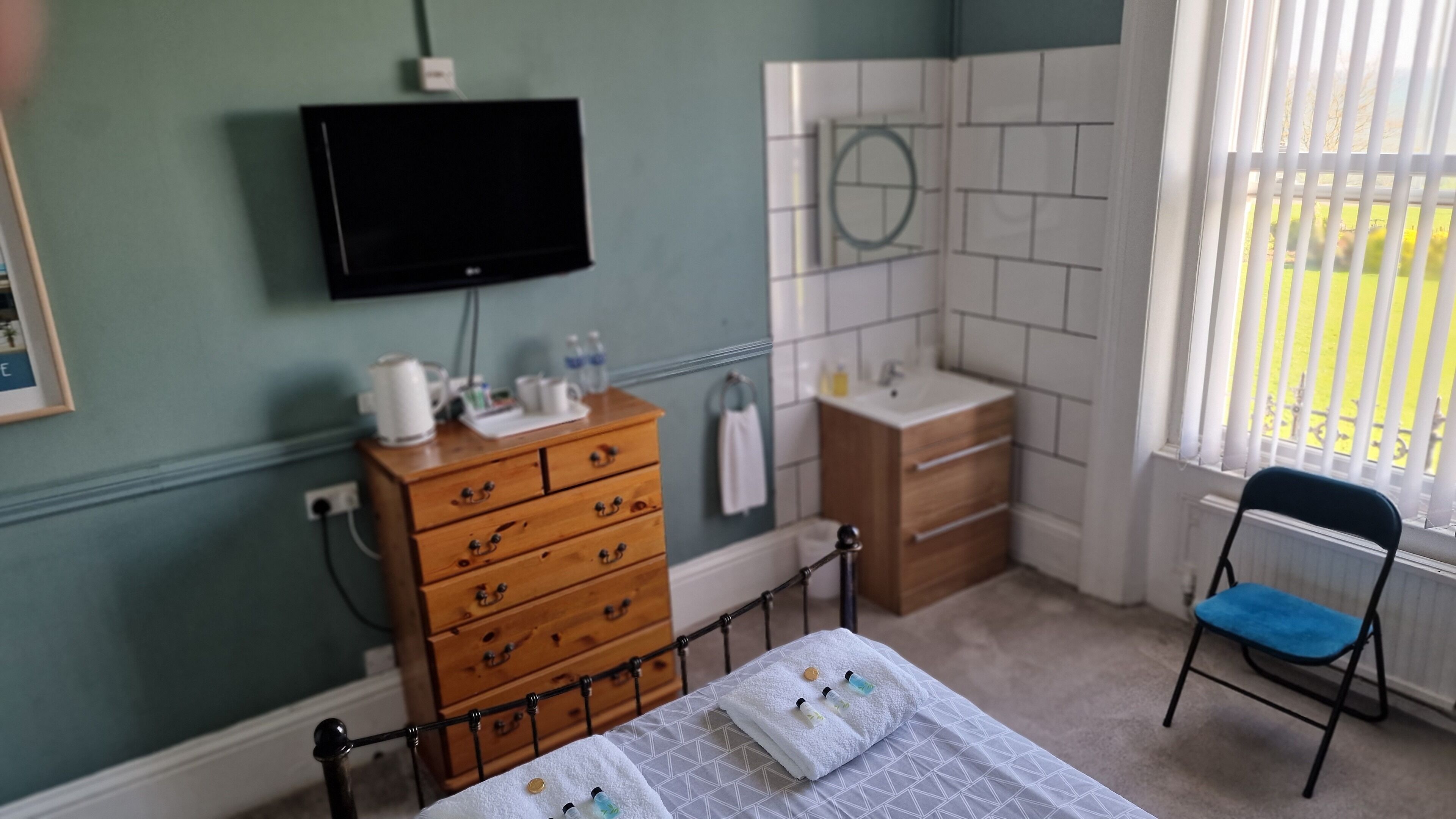 Ein Schlafzimmer mit einem Bett, einem Holzkasten, einem Fernseher und einem Fenster mit Jalousien.