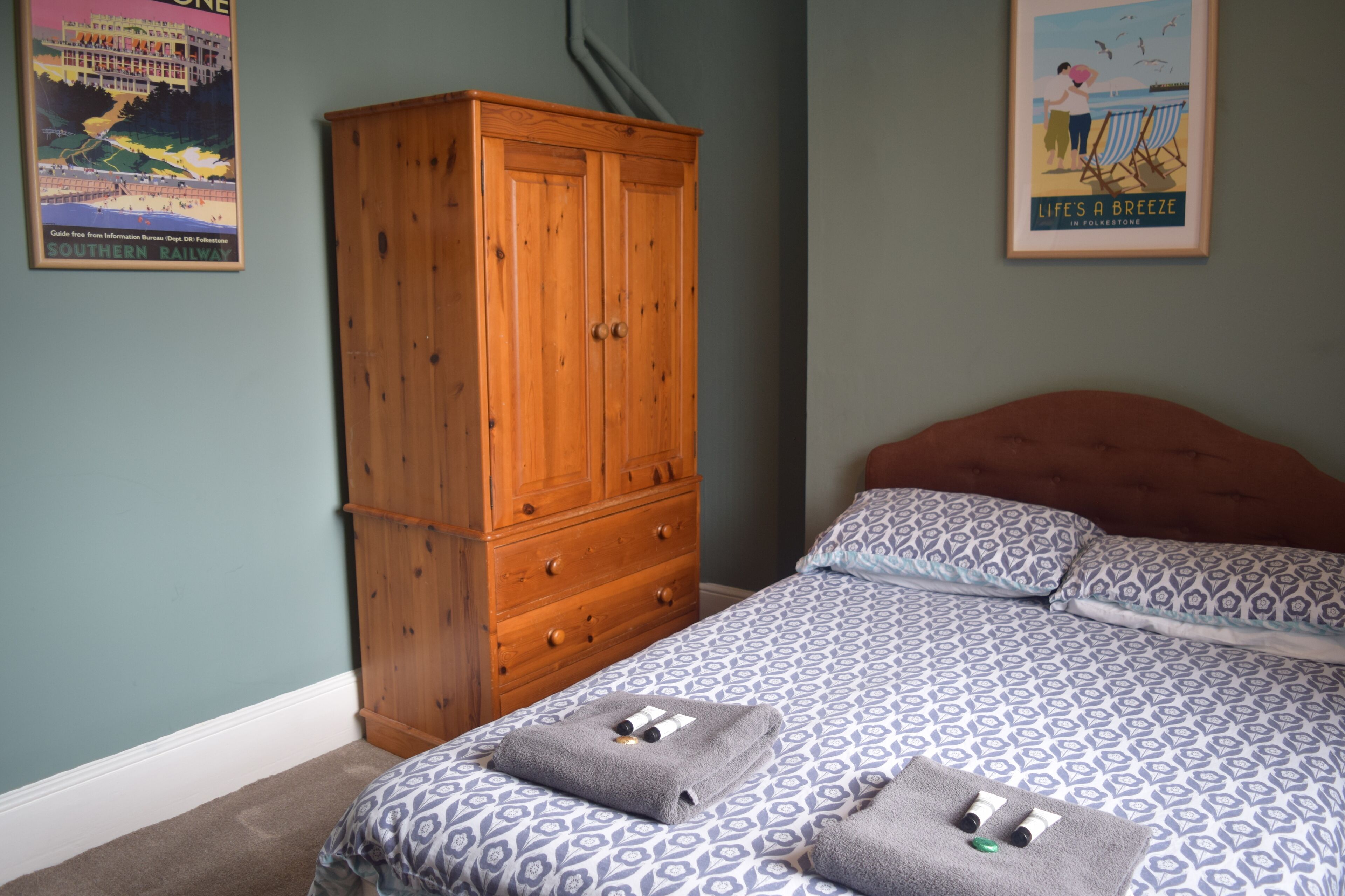 A bedroom with a bed, a wooden wardrobe, and two posters on the wall.