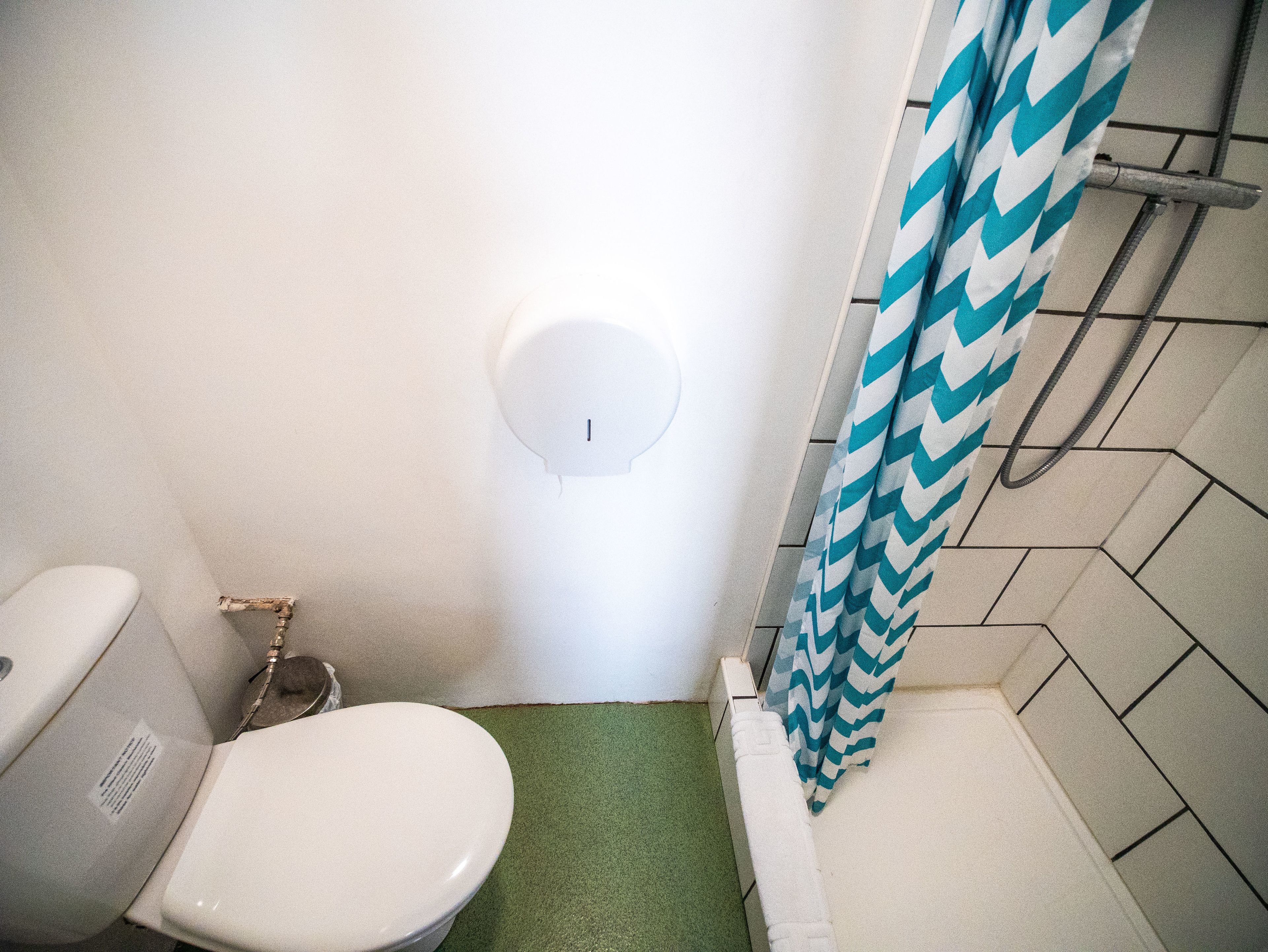 A small bathroom with a toilet, a shower with a blue and white chevron shower curtain, and a wall-mounted light fixture.