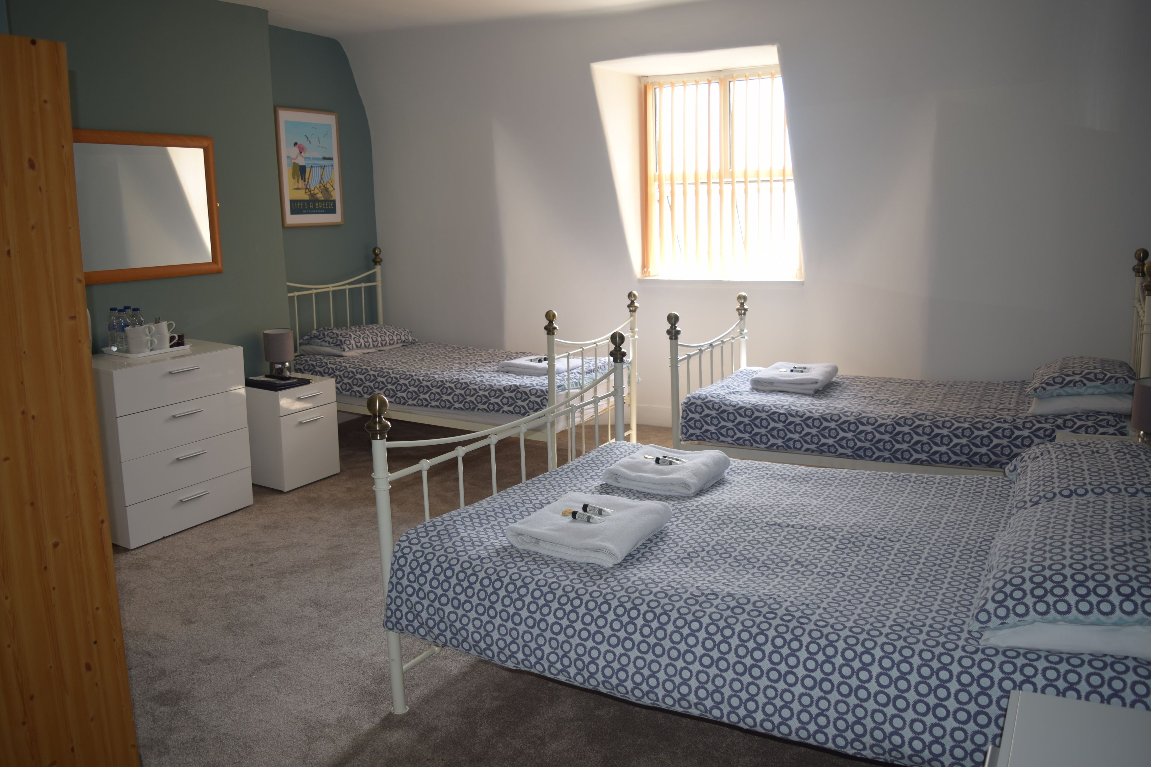 Un dormitorio con dos camas individuales, un aparador, un espejo y una ventana con persianas.