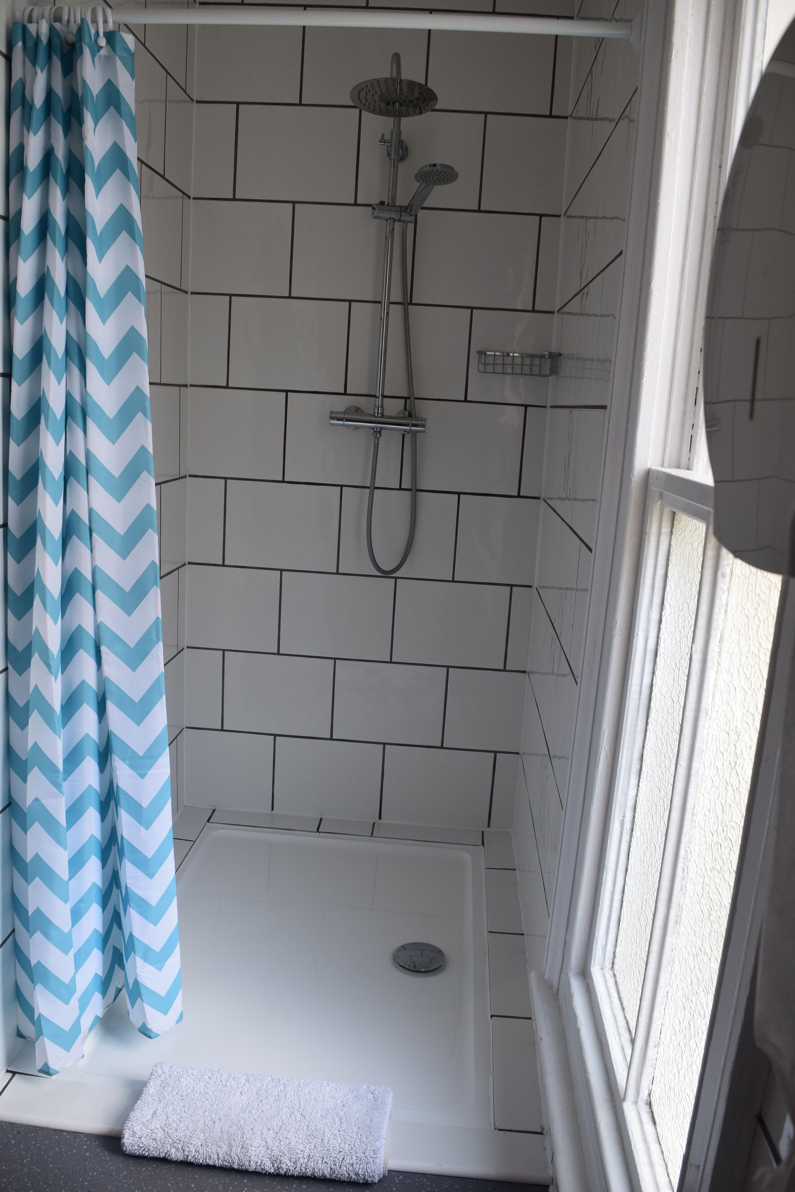 A shower area with a chevron-patterned shower curtain, a white bathtub, and a window to the right.