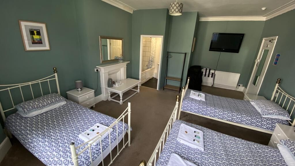 A bedroom with three single beds, a vanity with a mirror, a television on the wall, and a door leading to a bathroom.