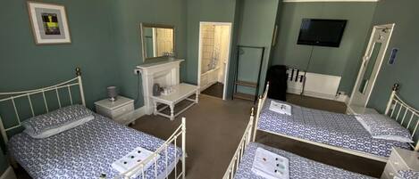 A bedroom with three single beds, a vanity with a mirror, a television on the wall, and a door leading to a bathroom.