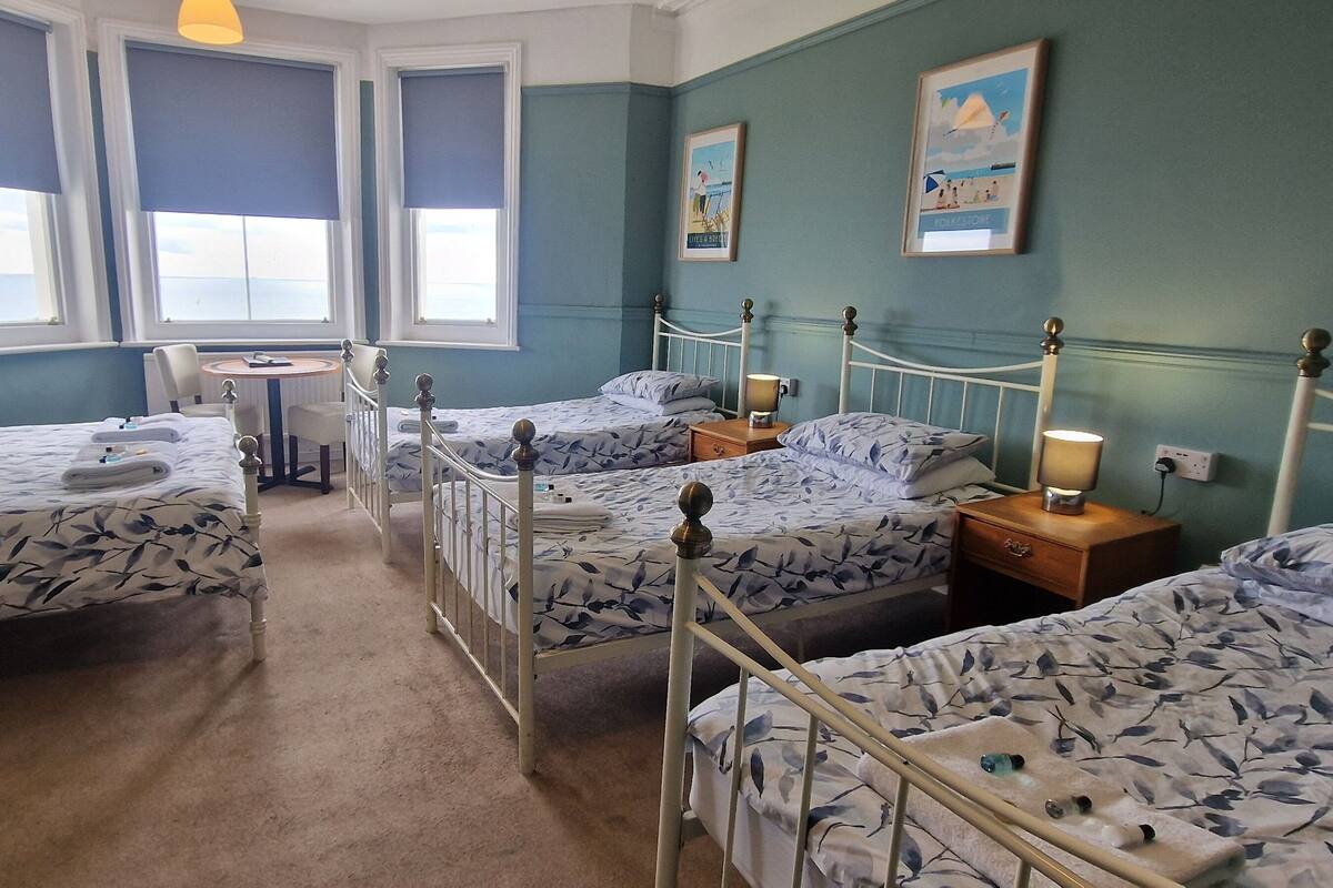 A hotel room with four beds, a small table, and a window with a view.