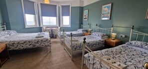 A hotel room with four beds, a small table, and a window with a view. - Westward Ho Hotel (Folkestone)