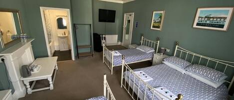 A room with three beds, a desk, a mirror, a television, and framed pictures on the wall.