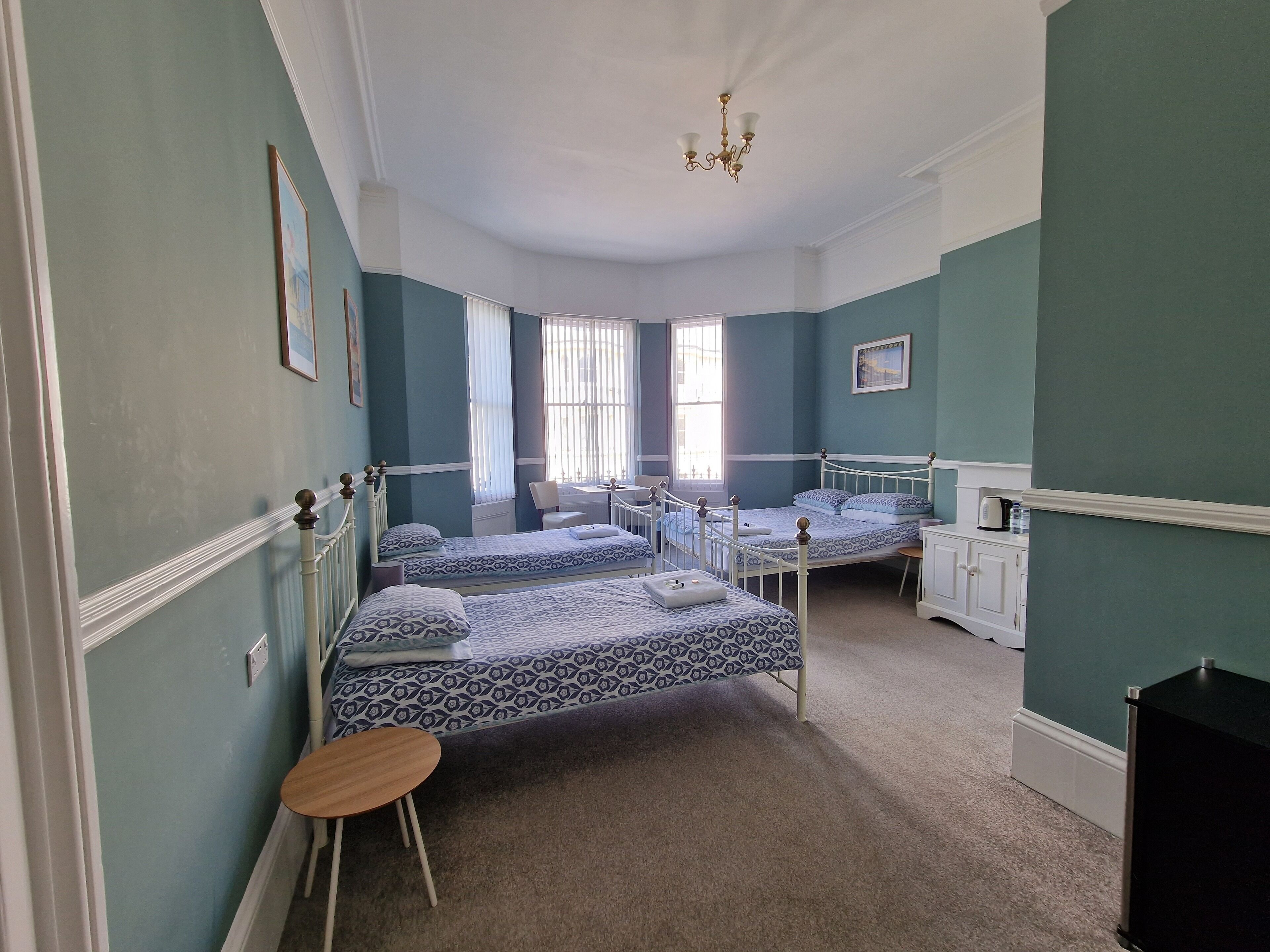A room with two single beds, a small table, a chair, a desk, and a cabinet.