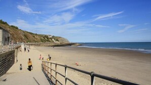 A sandy beach with a stone wall and a metal railing. - Westward Ho Hotel (Folkestone)