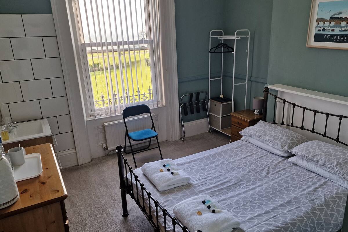 A neatly arranged bedroom with a bed, a chair, a small table, and a window with a view of the outside.