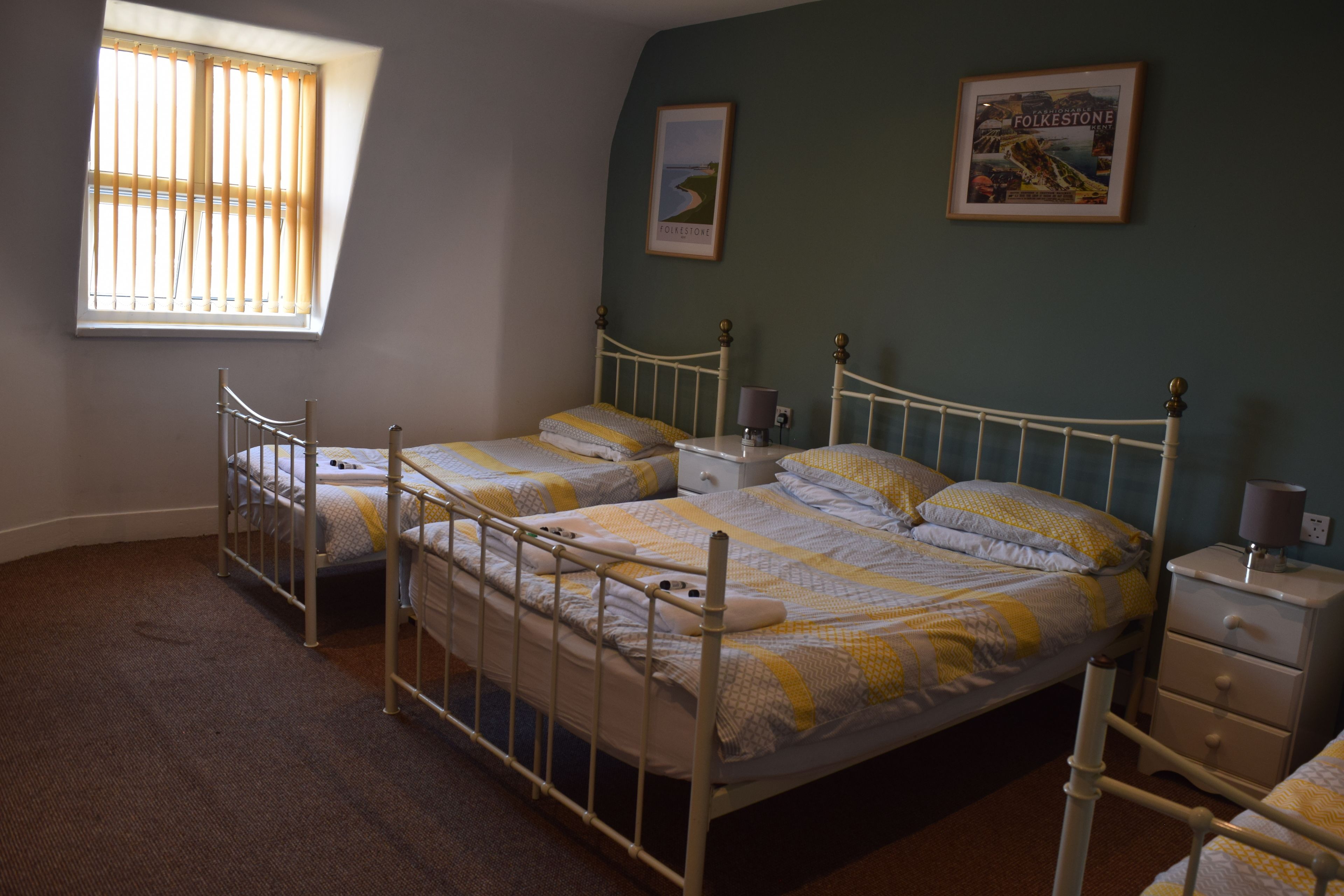 Een slaapkamer met twee bedden, een nachtkastje en een raam met zonwering.