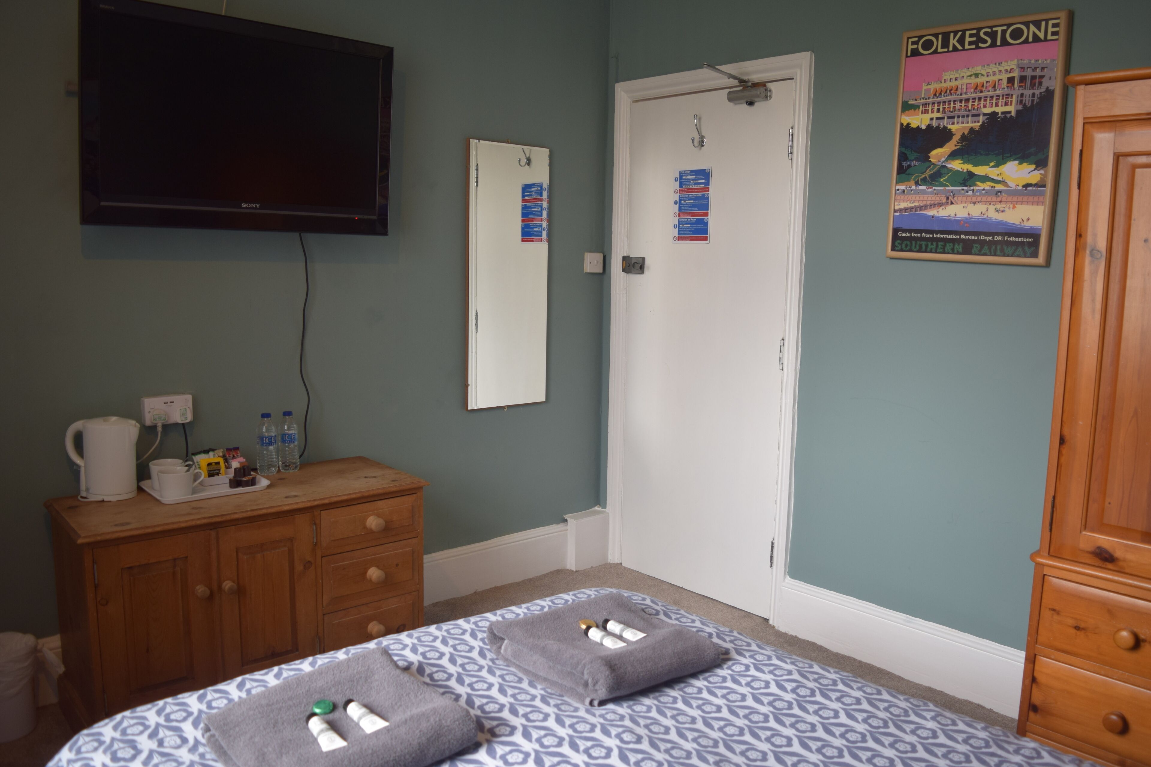 A bedroom with a bed, a dresser, a television, and a door with a poster.