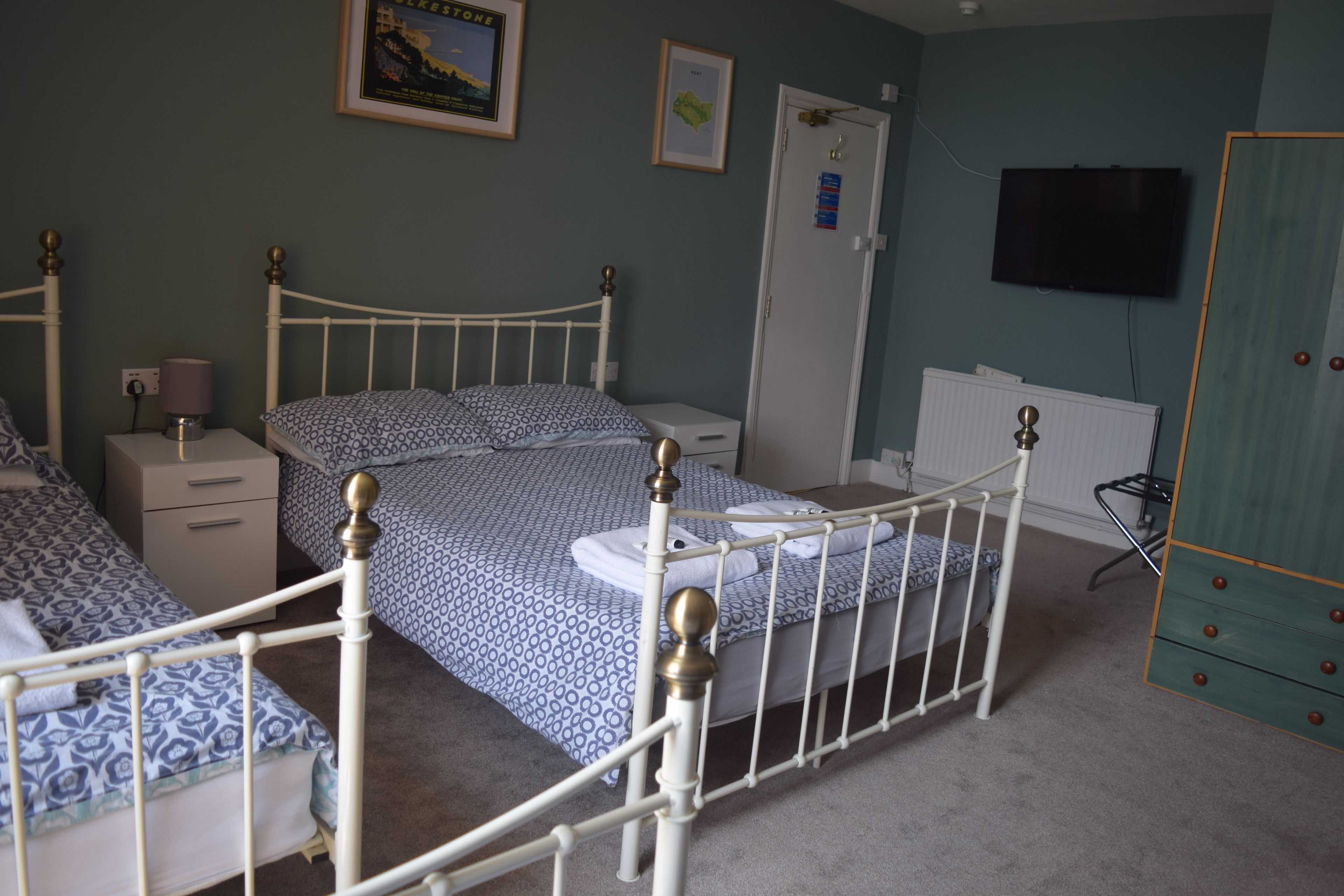 Un dormitori amb un llit individual, una tauleta de nit, un armari, una televisió i una porta amb un cartell.