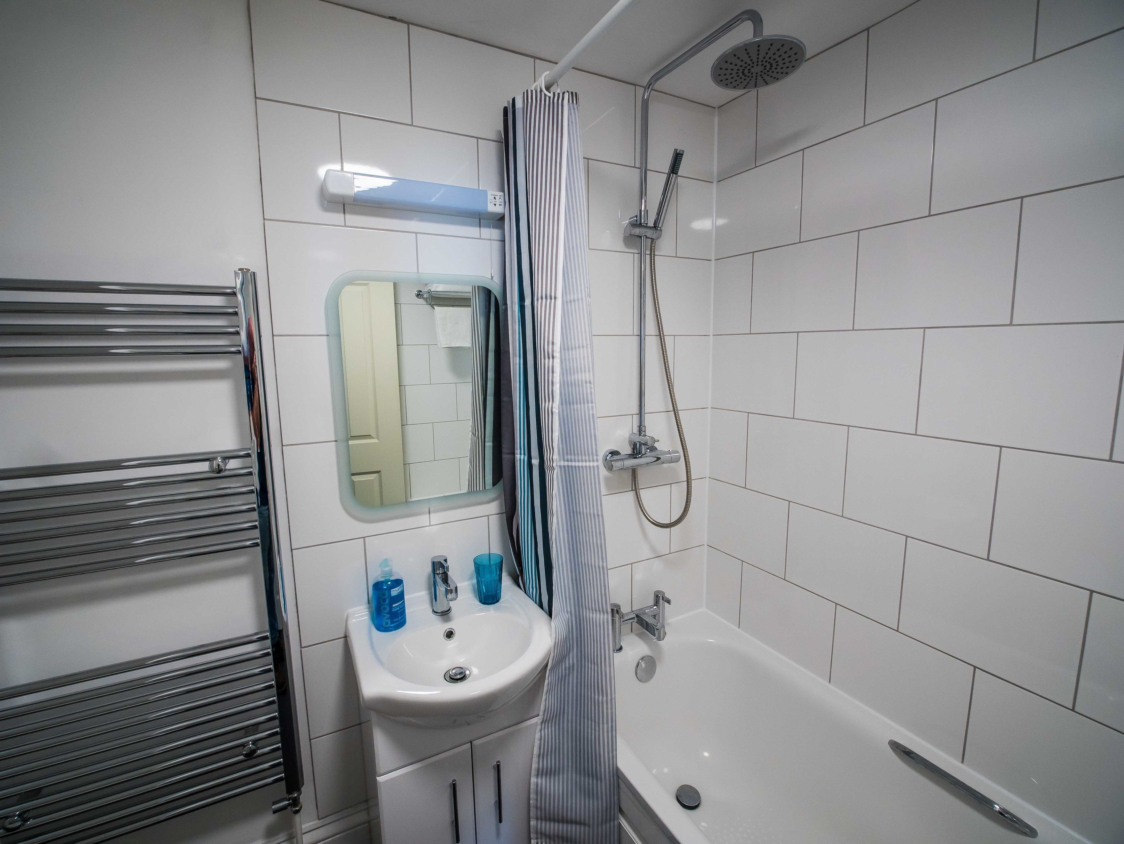 A bathroom with a white sink, a mirror, a shower, and a towel rack.