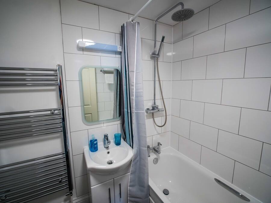 A bathroom with a white sink, a mirror, a shower, and a towel rack.