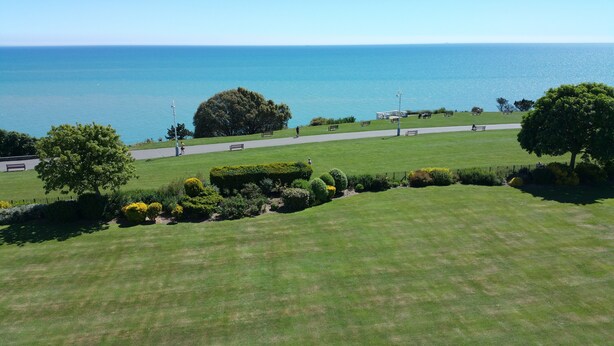 A well-maintained grassy area with a pathway leading to the sea, benches, and a statue. - Westward Ho Hotel (Folkestone)