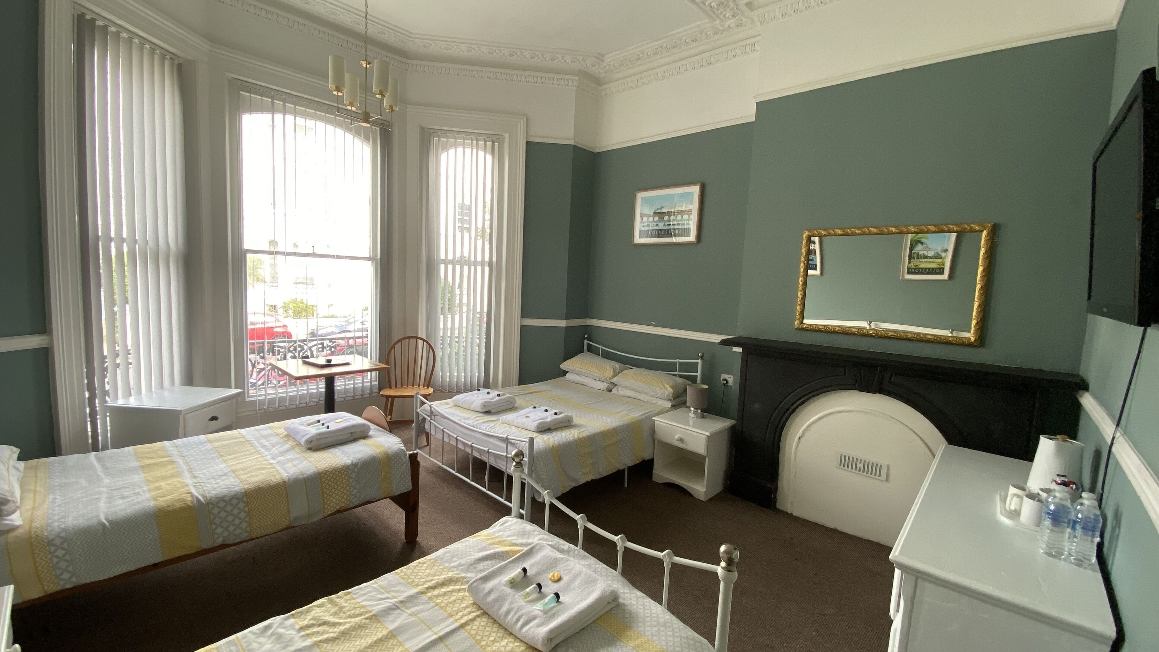 A hotel room with two single beds, a desk, a chair, a fireplace, and a window with blinds.