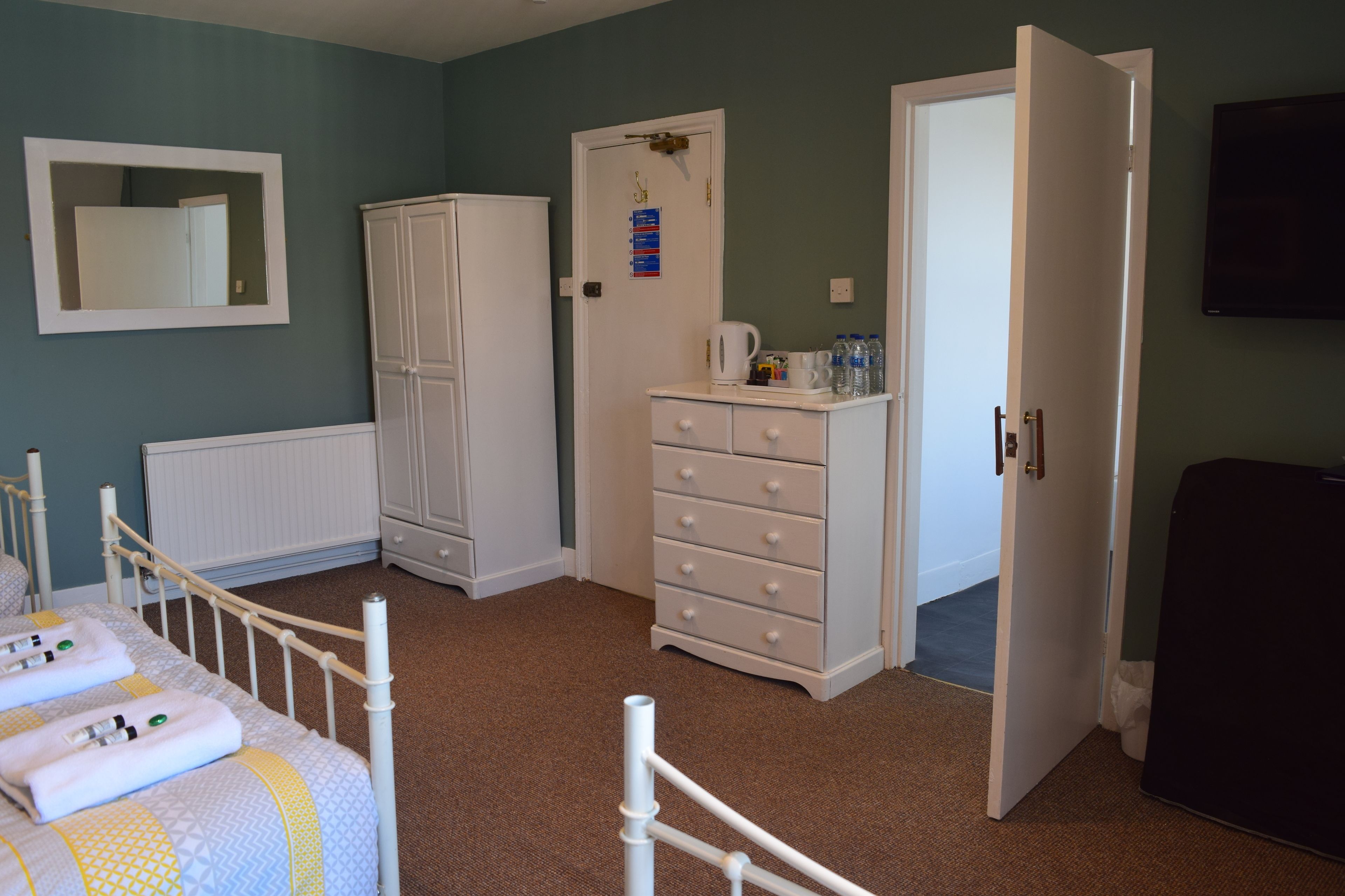 A bedroom with a bed, a wardrobe, a dresser, a radiator, and a television.
