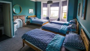 A room with four beds, a fireplace, a mirror, and large windows. - Westward Ho Hotel (Folkestone)