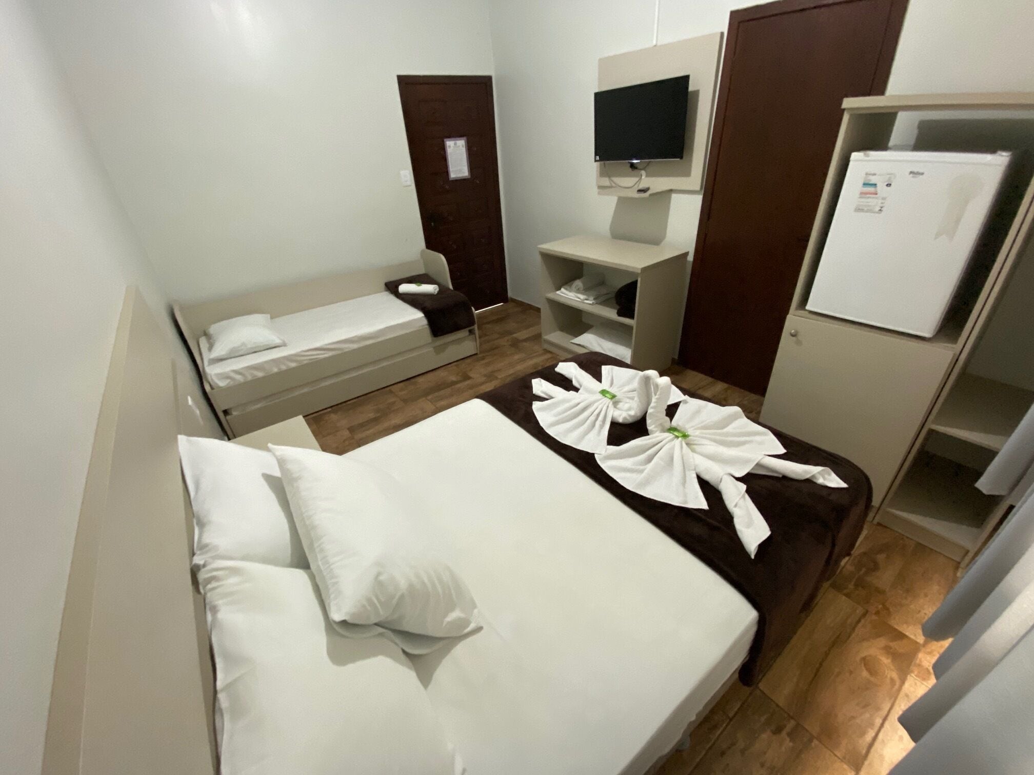 A hotel room with a single bed, a small desk, a television, and a minibar.