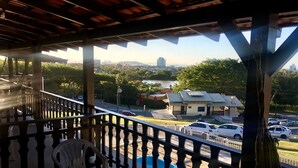 A covered outdoor area with a wooden ceiling, a white plastic chair, and a view of a parking lot and buildings in the distance. - Hotel Panorâmico (Penha)