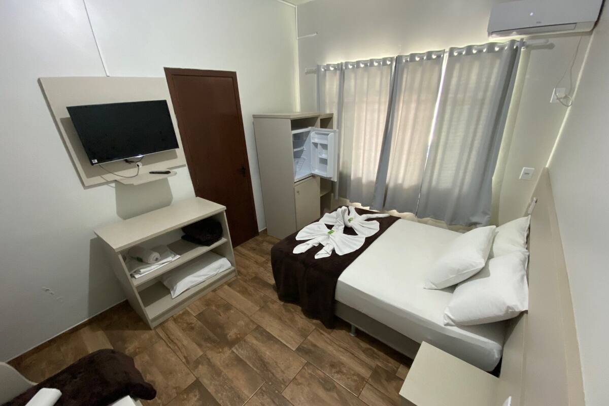 A compact hotel room with a bed, a TV mounted on the wall, a wardrobe, and a small desk.