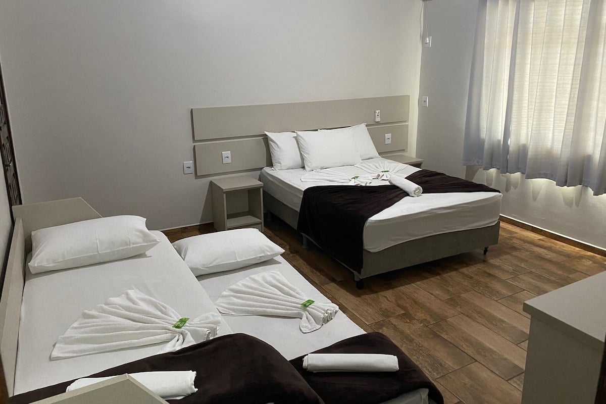 A hotel room with two beds, a nightstand, a bedside table, and an air conditioning unit.