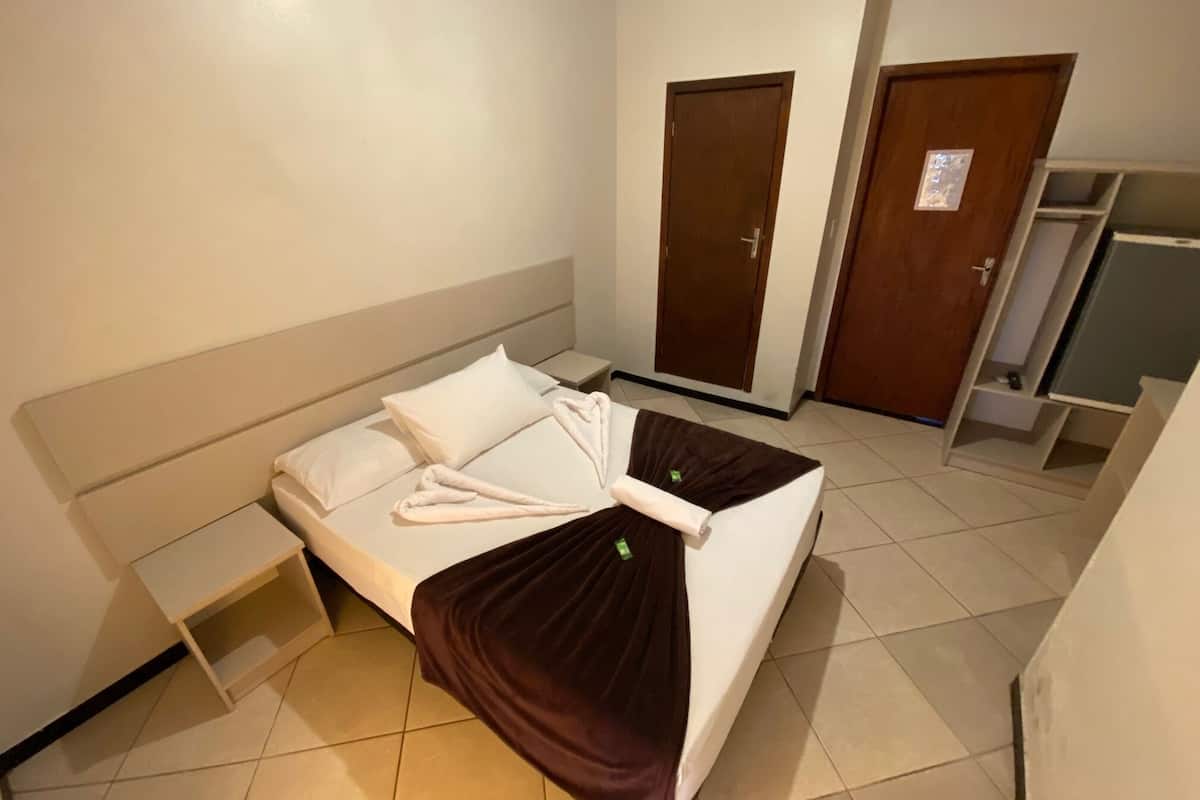 A small, neatly arranged hotel room with a single bed, a bedside table, and two doors.