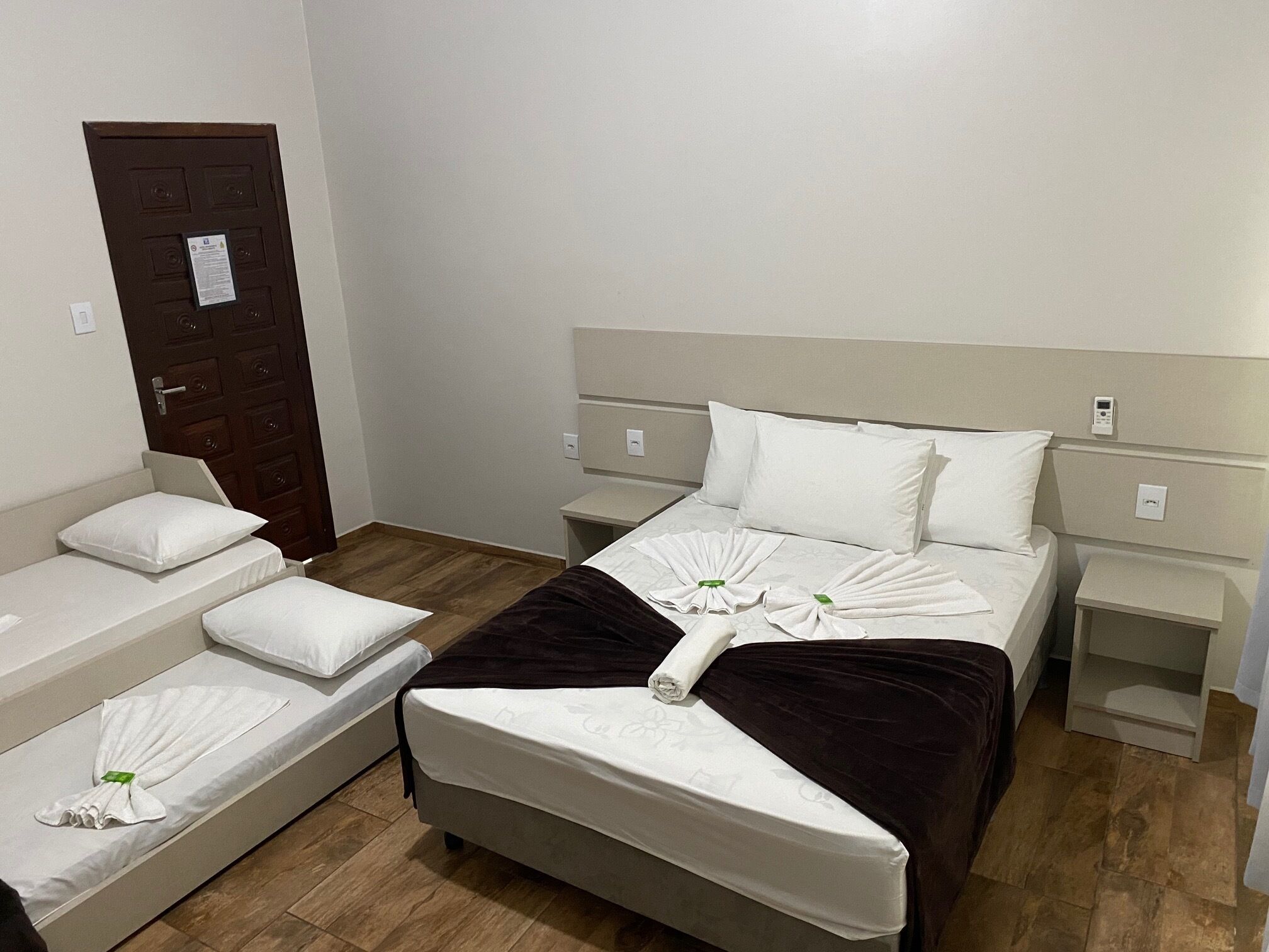 A hotel room with a large bed, two smaller beds, and a wooden door.