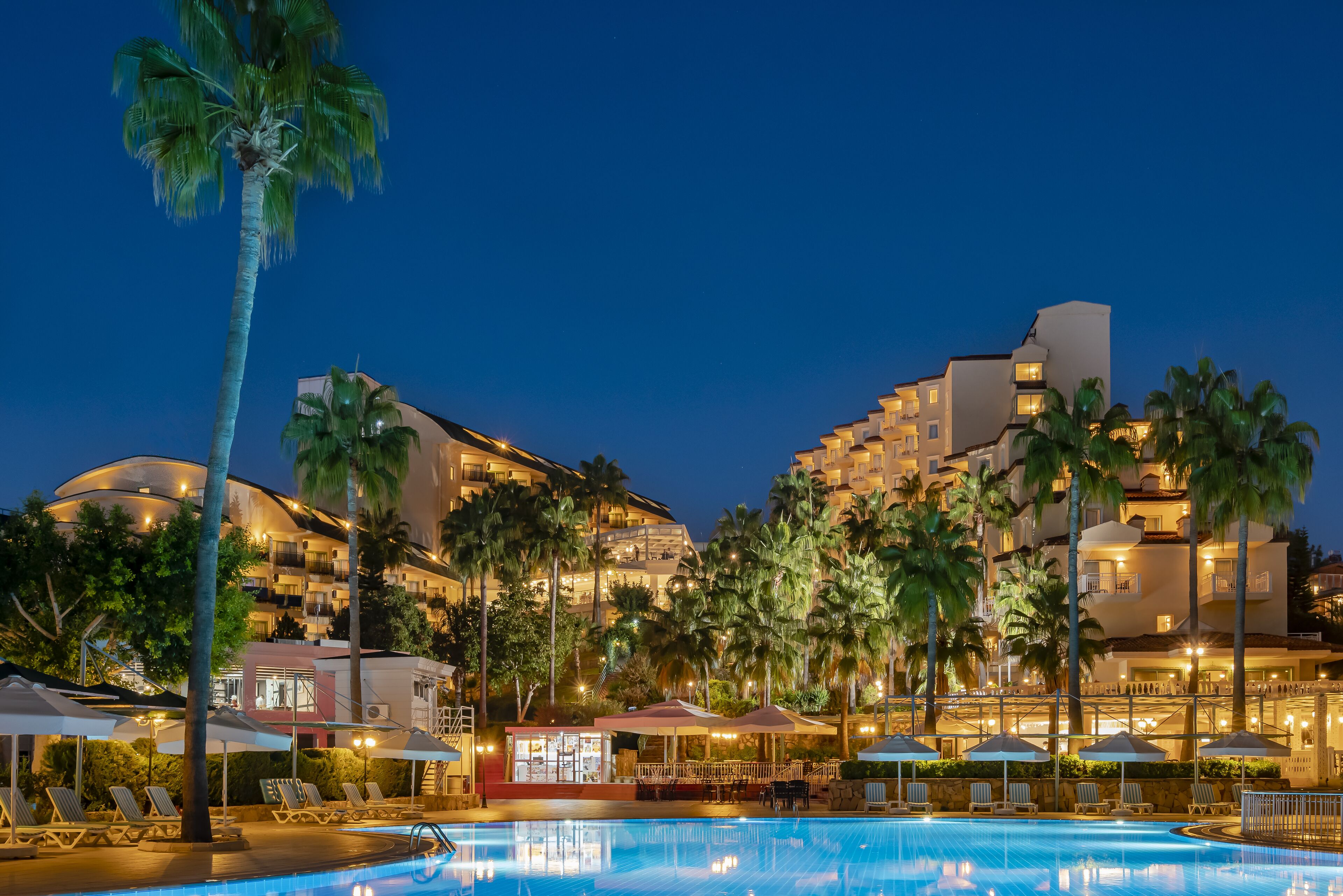 A hotel with a swimming pool, palm trees, and multiple balconies.
