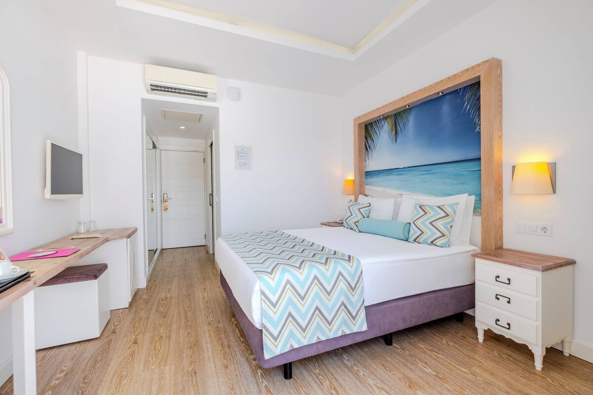 A bedroom with a bed, bedside table, and a painting of a beach scene.