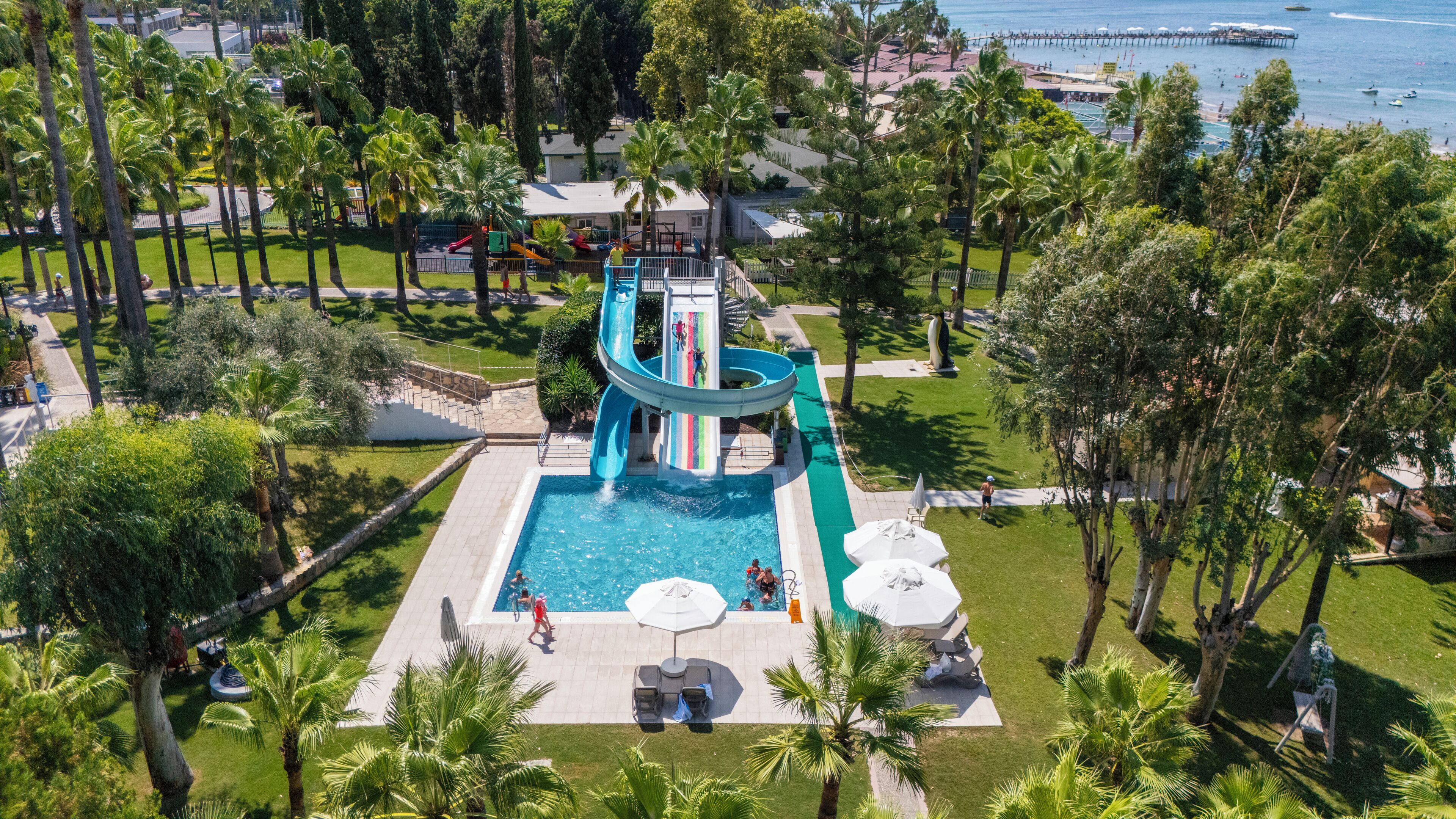 Un resort con piscina central, tobogán acuático y zona de playa.