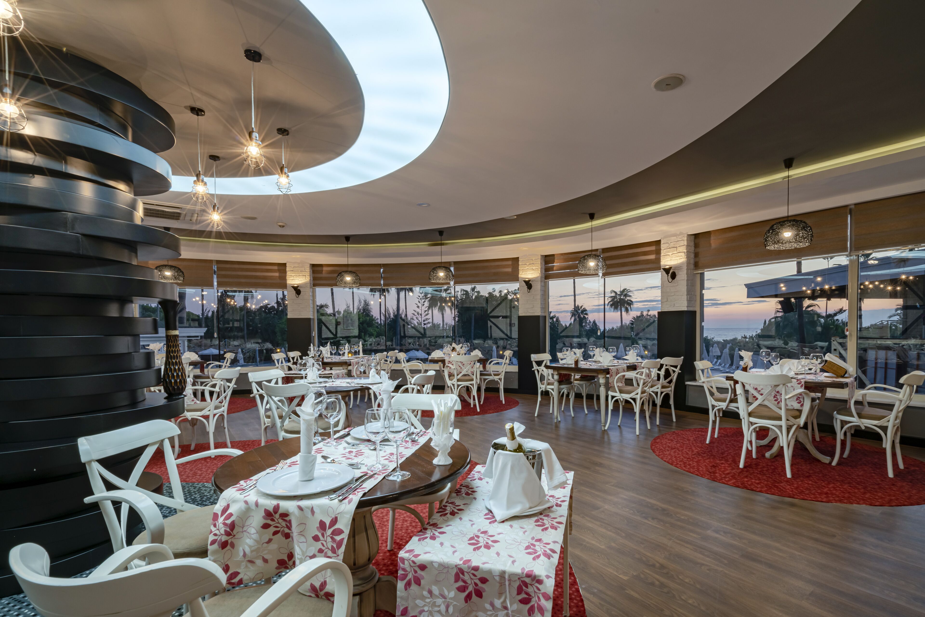 A restaurant with round tables, white chairs, and a view of the cityscape.
